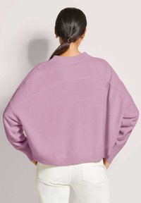Overmatige, lavendelkleurige gebreide trui met drop shoulders en geribbelde zoom. Zachte textuur, lange mouwen en een relaxte pasvorm. Gecombineerd met witte broek.