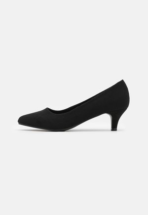 Zapatos de mujer de ante negro con tacón bajo, punta afilada y tacón kitten delgado, sobre un fondo blanco liso.