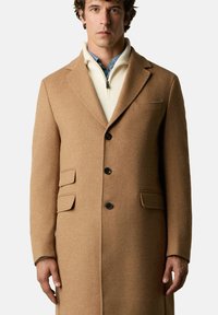 Kamelhaar-Mischwollmantel mit Reverskragen, drei vorderen Knöpfen, zwei vorderen Pattentaschen und einer einzelnen Brusttasche.