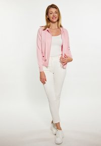 Heled roosa kapuutsiga cardigan, millel on pikad varrukad, kantud valge särk lahti, koos valgete sobivate pükstega ja valgete tossudega.