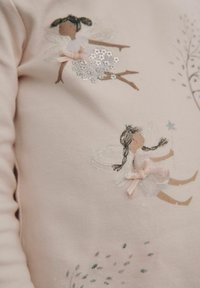Light pink long-sleeve top featuring two embroidered fairies with intricate details, sequins, and bows, set against a simple floral design.