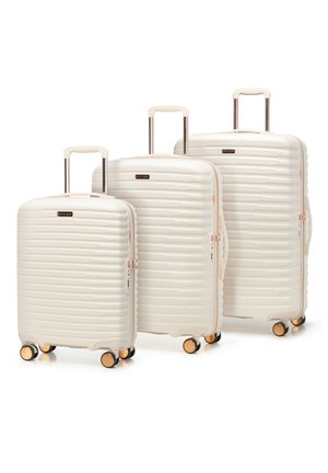 Trois valises rigides couleur crème, équipées de quatre roues et de poignées rétractables, disposées de la plus petite à la plus grande, sur un fond blanc.