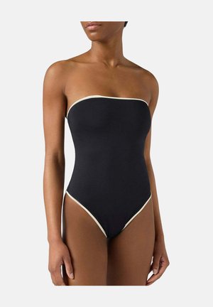 Femme portant un maillot de bain une pièce noir sans bretelles avec un liseré blanc le long du bord supérieur et des ouvertures des jambes.