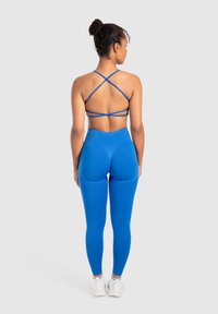 Reggiseno sportivo blu con spalline incrociate e leggings a vita alta coordinati. Tessuto morbido e elasticizzato con un design aderente.