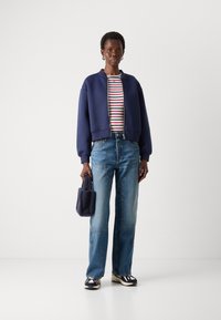 Navy cropped jacket, striped shirt with red and white lines, blue wide-leg jeans, navy fuzzy bag, and black and white sneakers.