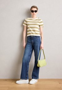 Striped olive and cream crop top, blue wide-leg jeans, white sneakers, and a small textured green handbag. Sunglasses complete the look.