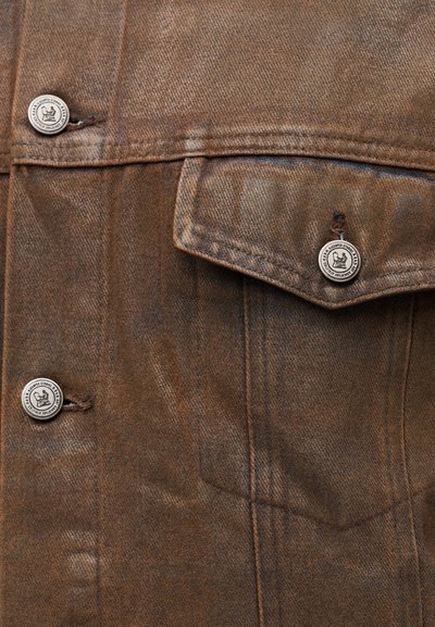 Καφέ τζιν μπουφάν με ραφές σε αντίθεση, ασημένια κουμπιά και τσέπη στο στήθος. Ομαλή υφή με στιβαρό σχεδιασμό.