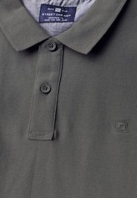 Polo shirt gris foncé avec un tissu texturé, fermeture à deux boutons et un petit logo brodé sur le côté gauche. Design simple avec un col.