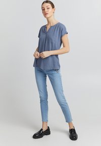 Haut bleu à manches courtes avec un décolleté en V, une poche poitrine et une coupe décontractée; associé à un jean skinny bleu clair et des mocassins noirs.