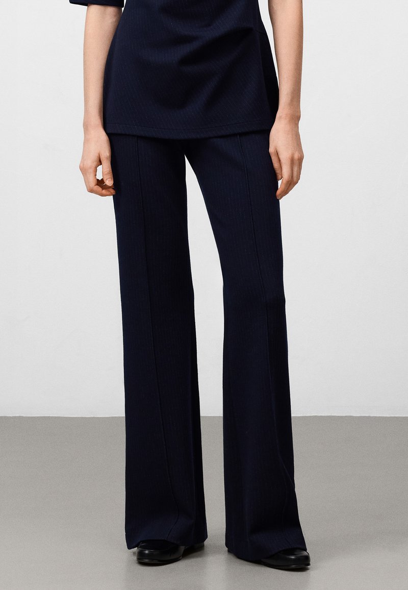 Navy wijde broek in een gestructureerde stof met verticale streepjes. Heeft een hoge taille en gestructureerde pasvorm, gecombineerd met zwarte schoenen.