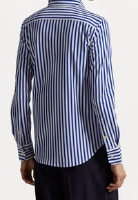 Niebiesko-biała koszula w paski z kołnierzykiem zapinanym na guziki, długimi rękawami i zaokrąglonym dołem. Materiał wydaje się lekki o gładkiej fakturze.