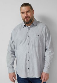 Lichtgrijs overhemd met knopen, gemaakt van stof met een subtiel patroon. Voorzien van een borstzak en donkere knopen. Lange mouwen.