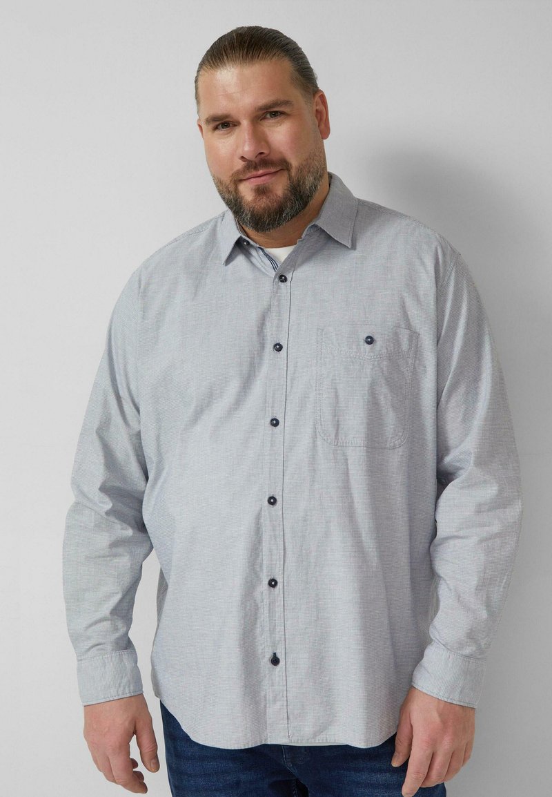 Lichtgrijs overhemd met knopen, gemaakt van stof met een subtiel patroon. Voorzien van een borstzak en donkere knopen. Lange mouwen.