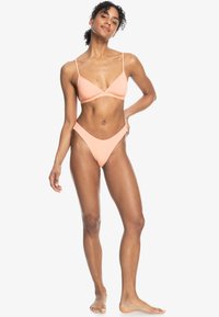 Perzikkleurige bikini set met een driehoekig topje met dunne bandjes en een hoog-was-broekje. Gladde textuur, minimalistisch ontwerp en geen patronen.