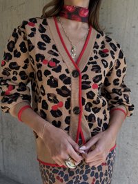 Beżowy kardigan w cętki z czerwoną akcentacją; ma hafty w kształcie wiśni, ściągacze na mankietach oraz zapięcie na guziki.