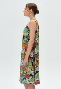 Ärmelloses, tropisch gemustertes Kleid in Schwarz, mit leuchtend grünen, orangefarbenen und weißen Blättern sowie einem lockeren, fließenden Schnitt.