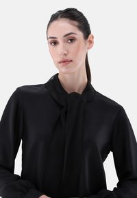 Black blouse with a neck tie, made of a smooth fabric. Features long sleeves and a classic design, softly draping around the neckline.