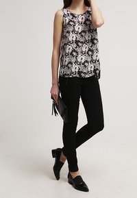 Top senza maniche bianco e nero con motivo floreale, abbinato a pantaloni neri slim-fit e mocassini neri, completato da una piccola borsa a mano nera.
