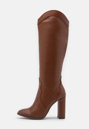 Botte haute en cuir marron avec bout pointu, talon bloc haut et détails festonnés sur la tige et le pied.