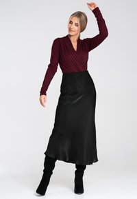 Bordowy top z długim rękawem w białe kropki oraz głębokim dekoltem w serek, zestawiony z czarną satynową maxi spódnicą i czarnymi kozakami za kolano.