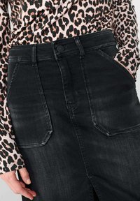 Zwarte jeansrok met voorzakken, een knoopsluiting en een getailleerde pasvorm. Gepaard met een roze panterprint top.