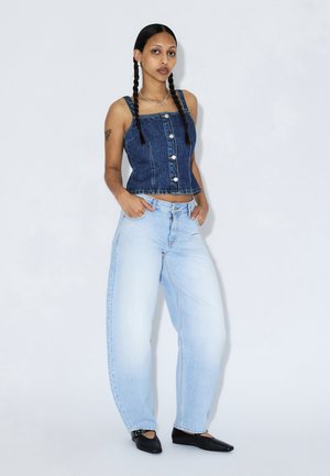Denim cropped top med knaplukning og frynset kant, kombineret med lyseblå oversized jeans; iført sorte flade sko med en glat tekstur.