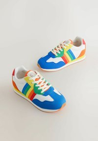 Värikkäät tennarit, joissa on sininen synteettinen päällinen, valkoiset paneelit, moniväriset raidat ja kumipohjat. Varustettu nauhoilla ja pyöreällä kärjellä.