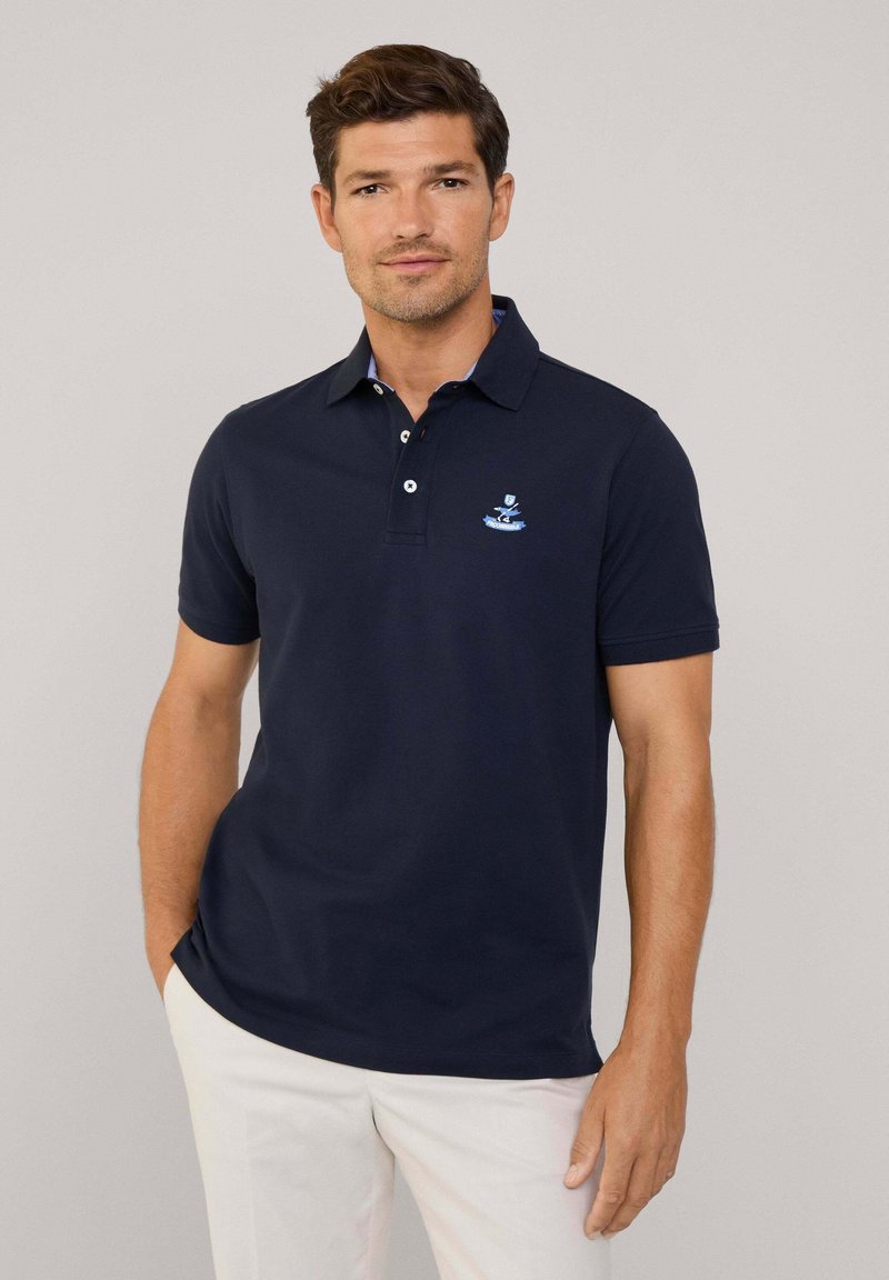 Polo shirt blu navy con colletto, patta con tre bottoni e logo ricamato. Tessuto di cotone morbido con maniche corte e vestibilità classica.