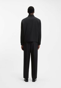Svart jacka och byxor tillverkade av slätt tyg. Jackan har krage och rak passform, med enkel design utan synliga utsmyckningar.