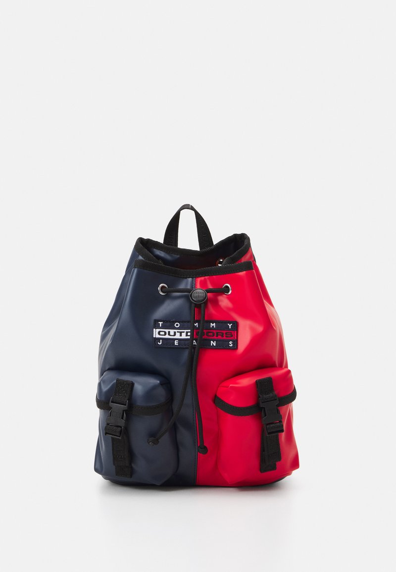 Backpack featuring a split design in red and navy blue, made from glossy material, with two front pockets and a drawstring closure.