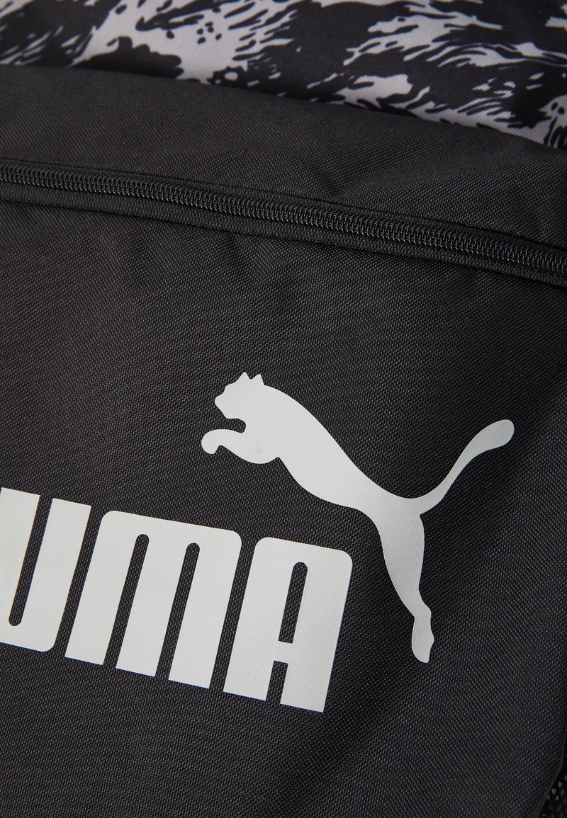 Sac à dos en tissu noir arborant un logo Puma blanc bien en vue et une inscription audacieuse, avec un compartiment zippé et une surface texturée.