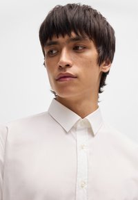 White collared shirt with a smooth, textured fabric, featuring a button-down front and standard collar, displayed on a model against a light background.