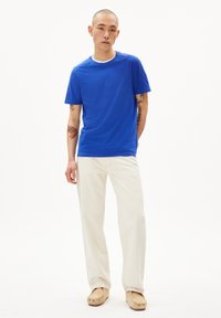 Königsblaue Baumwoll-T-Shirt mit Rundhalsausschnitt, kombiniert mit crèmefarbenen weiten Hosen und beigen Slippern. Minimalistisches Design.