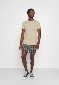 Beige tričko s logem, černobílé kostkované šortky a černé vysoké tenisky. Model má na sobě oranžové sluneční brýle.