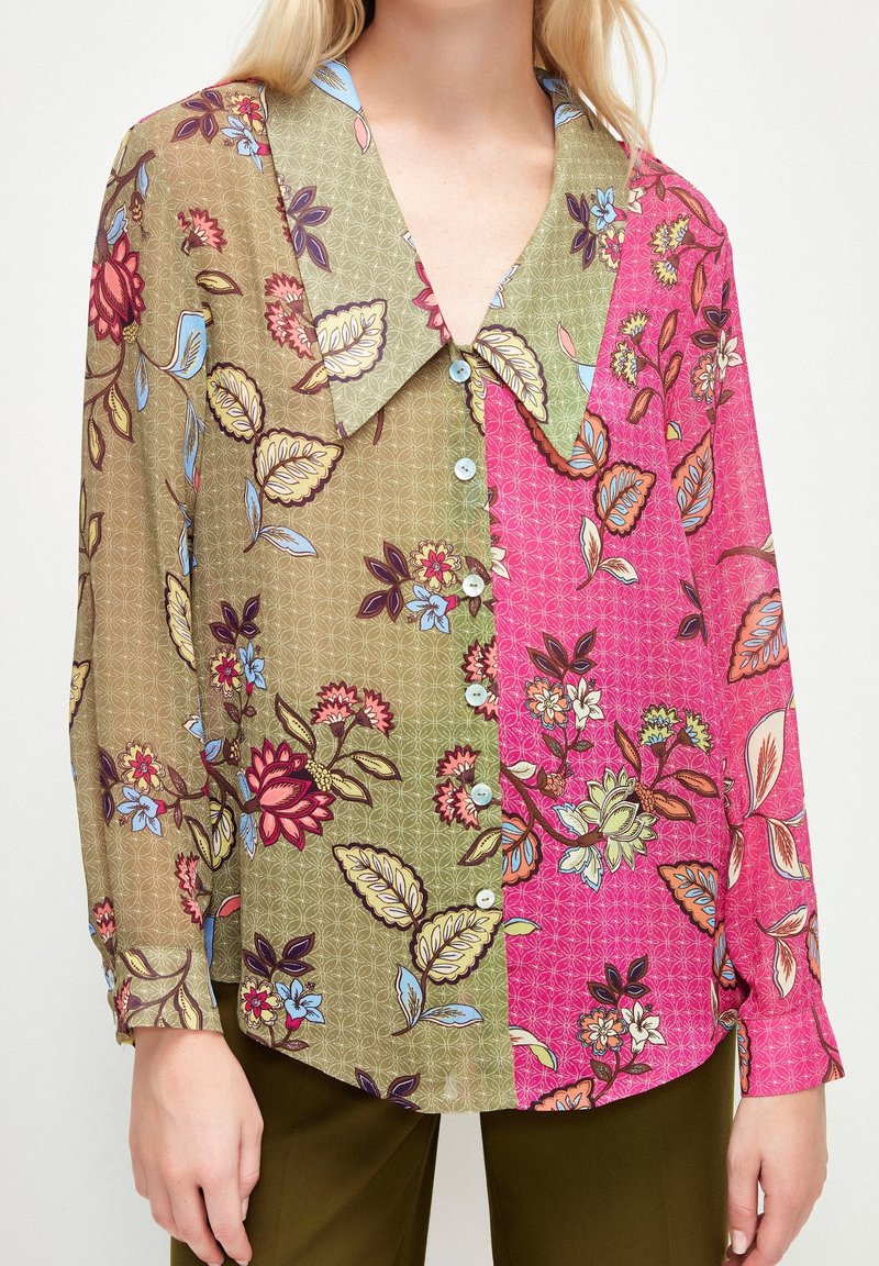 Chemise à imprimé floral présentant un design dédoublé avec des sections vertes et roses, un large col, et des boutons sur le devant. Le matériau est léger.