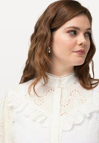Witte geborduurde blouse met een gerimpelde kraag, knoopsluiting en ingewikkelde bloemmotieven. Lichtgewicht stof met een gestructureerde uitstraling.