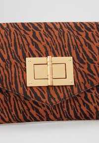 Pochette à motif tigre marron et noir avec fermeture à loquet rectangulaire doré sur fond blanc.
