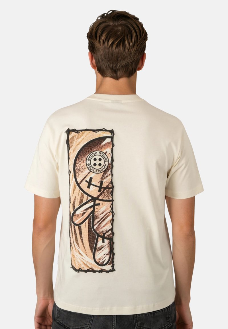 Man wearing cream-colored T-shirt with vertical rectangular graphic of a stylized figure with button eye and crossed-out eye on the back.