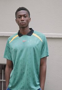 Polo shirt vert Nike avec un col noir, présentant un motif subtil et des accents jaunes sur les épaules, porté avec un jean bleu.