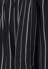 Černá tkanina s bílými vertikálními pruhy, s texturovanou vazbou. Obsahuje sklady pro objem.