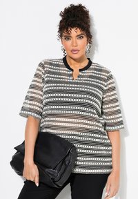 Stribet top i sort og hvid med en klapkrave, korte ærmer og tekstureret stof. Modellen holder en sort læder clutch.