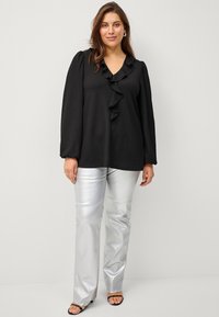 Black long-sleeve top with a V-neck and ruffled front, paired with shiny silver wide-leg pants. Featuring soft, textured fabric and simple black sandals.