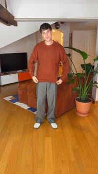 Rustfarvet strikket sweater med ribbet struktur, kombineret med grå løstsiddende bukser og hvide sneakers, mod et hjemligt interiør.