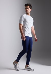 Lichtgrijs, nauwsluitend sportshirt, marineblauwe legging en zilveren hardloopschoenen. Het shirt heeft korte mouwen; de leggings zijn glad en rekbaar.