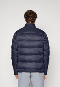 Marineblå puffjakke med quiltet design, høy krage, glatt tekstur og elastiske mansjetter. Ingen synlige logoer eller detaljer.