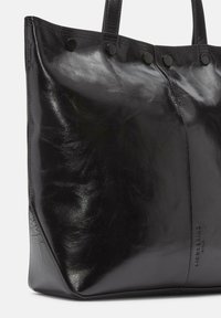 Czarna skórzana torba tote o gładkiej teksturze, z wyraźnym kształtem, z detalami w postaci zatrzasków oraz wytłoczonym logo marki na boku.