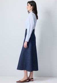 Světle modrá košile s dlouhými rukávy a manžetami na knoflíky, kombinovaná s tmavě modrou áčkovou sukní z denimu. K tomu jsou obuty ploché hnědé boty s špičatou špičkou.
