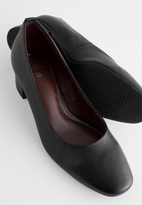 Paire de chaussures pour femmes en cuir noir à talons bas, bouts arrondis et semelles en caoutchouc texturées, présentées sur fond blanc.