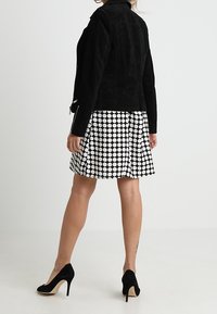 Svart mockajacka, figursydd design, parat med en svart och vit prickig klänning. Utseendet kompletteras av svarta högklackade skor.