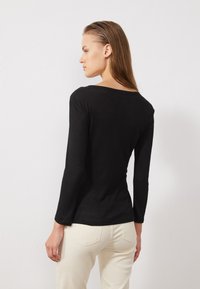 Haut noir à manches longues côtelé avec un décolleté large et une silhouette ajustée. Le tissu a une texture subtile, associé à un pantalon clair.